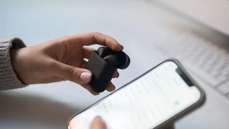 A person holding wireless earphones and a phone