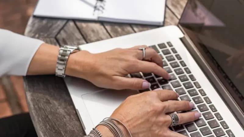 Hands typing on a laptop beside a notebook